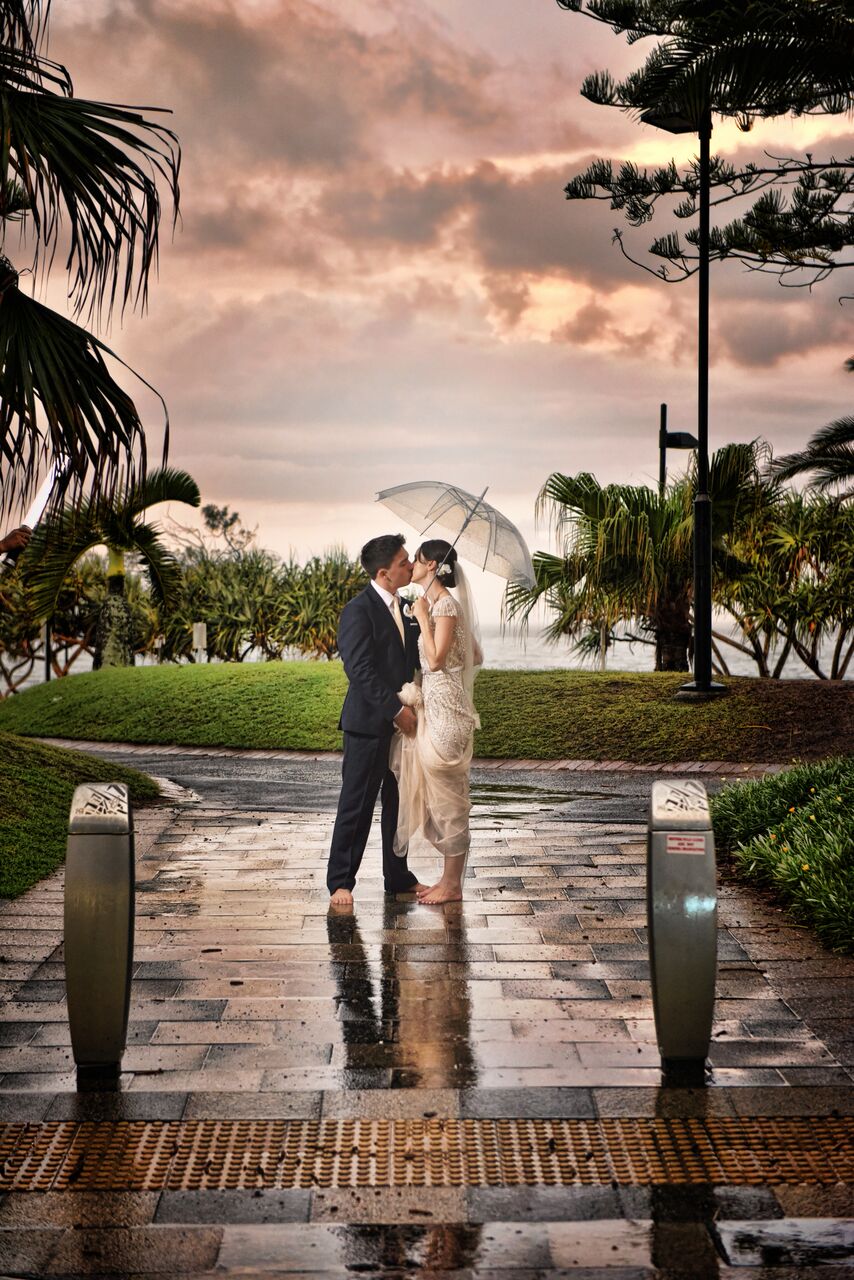 Bride and groom kissing under umbrella with ocean in background