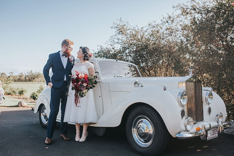 Bride and Groom pose in front of a white, classic Rolls Royce.