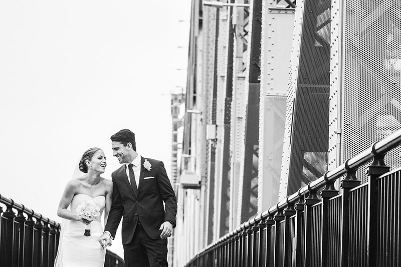 Bride and Groom happily laughing while walking across a bridge.