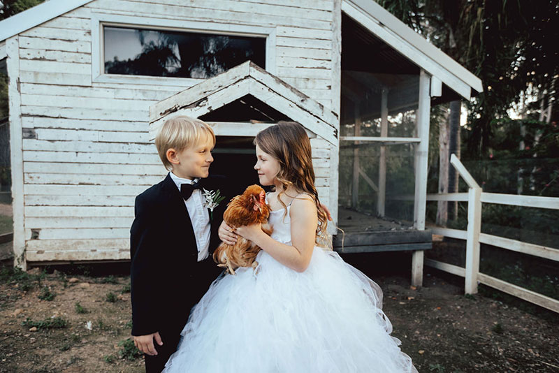 Photo by DK and Co. Photography of kids at wedding holding chook in chook pen.