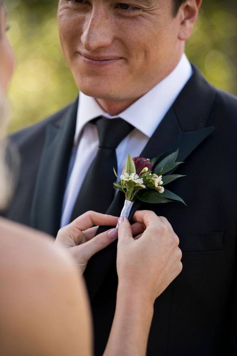 Photo taken by Leigh Warner Weddings of a Groom looking at Bride while she fixes the flower on his suit..