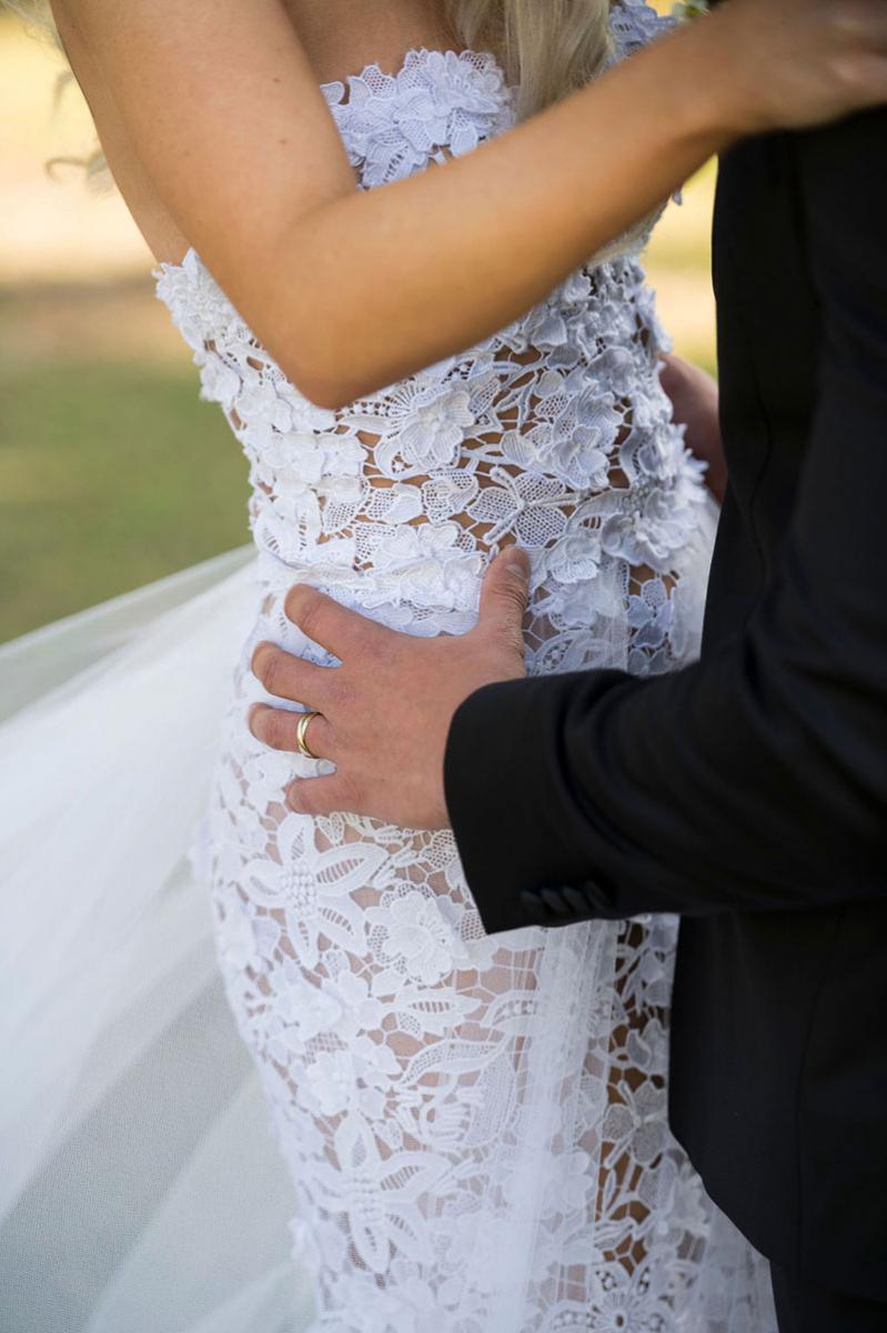 Photo taken by Leigh Warner Weddings of a Bride in a lace gown with the Grooms hands on her hips.