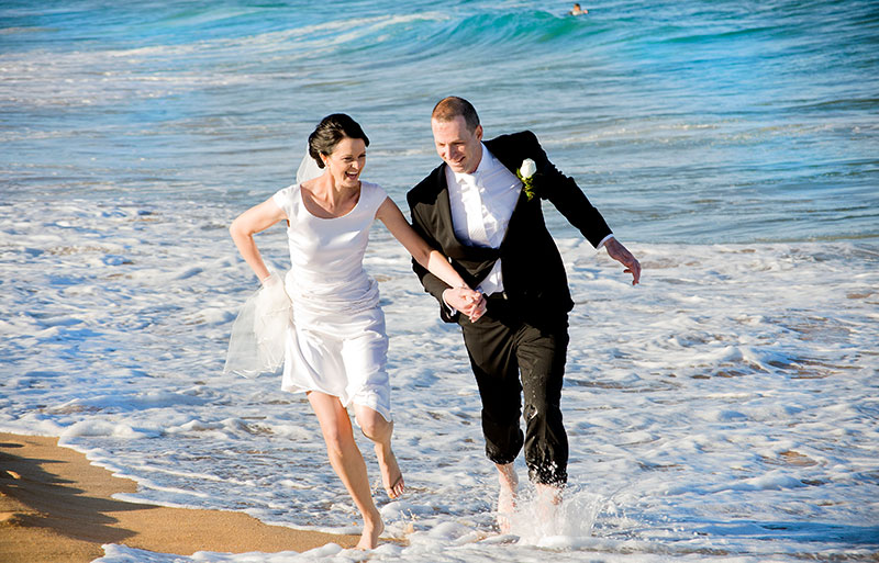 Happy bride and groom running through the water at the beach.
