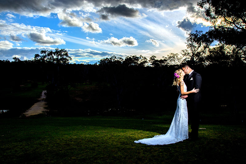 Bride and groom kissing under a vast blue sky at dusk..