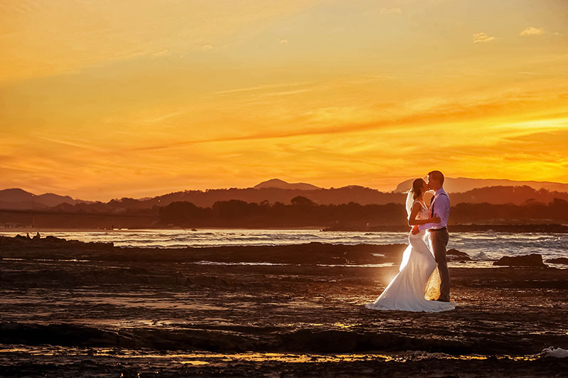Bride and groom together on beach with golden sunset.