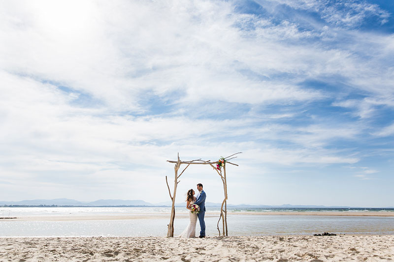 Bride and groom under a simple arbour on beach.