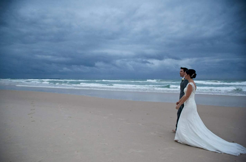 Bride and groom at the beach under a threatening sky.