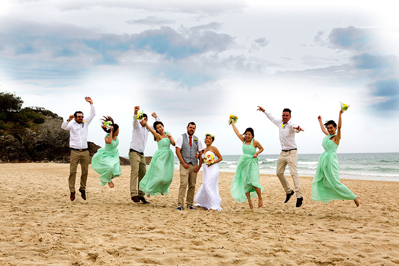 Happy wedding party with bright green dresses on beach.