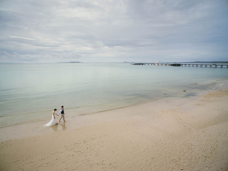 Bride and groom walking on a beautiful calm beach.