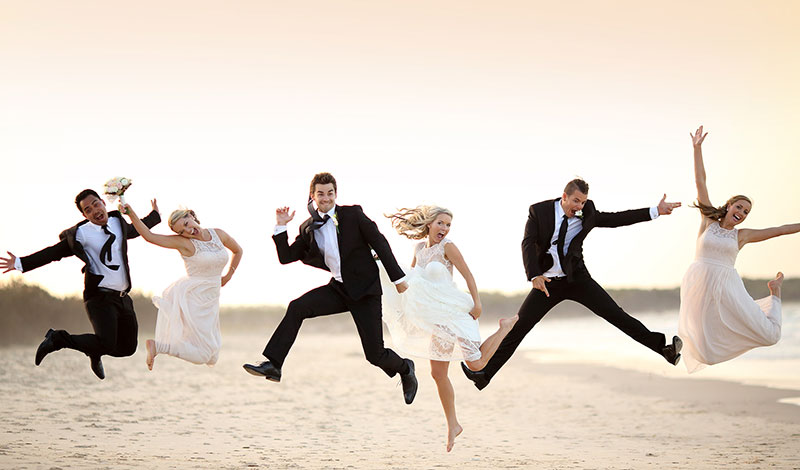 Wedding party jumping for joy at beach.