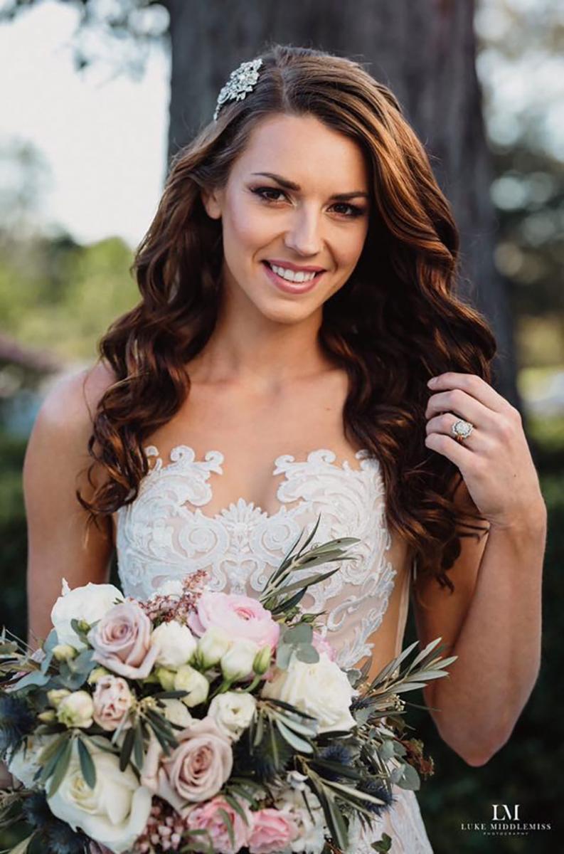 Bride with natural makeup holding flowers and smiling.