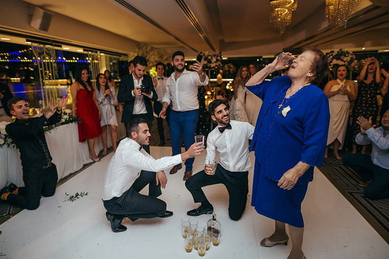 Grandma at wedding enjoys drinks with groom on dance floor. 