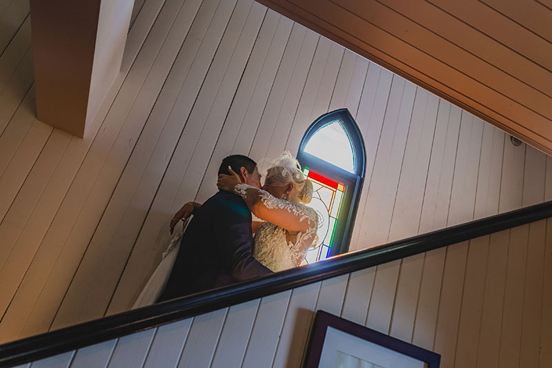 Bride and groom kiss in front of stained glass window at Broadway Chapel.