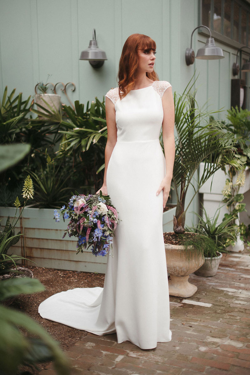 Red haired bride holding blue flowers wearing a sleek wedding dress.