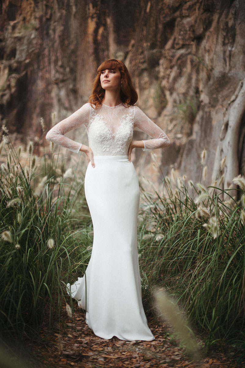 Red haired bride wearing a long sleeved wedding dress in outside location.