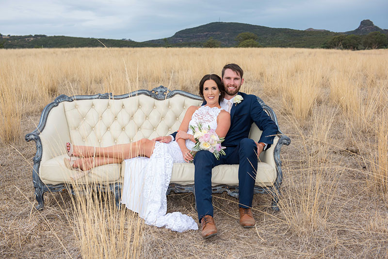 Bride and groom on vintage chair in a field.