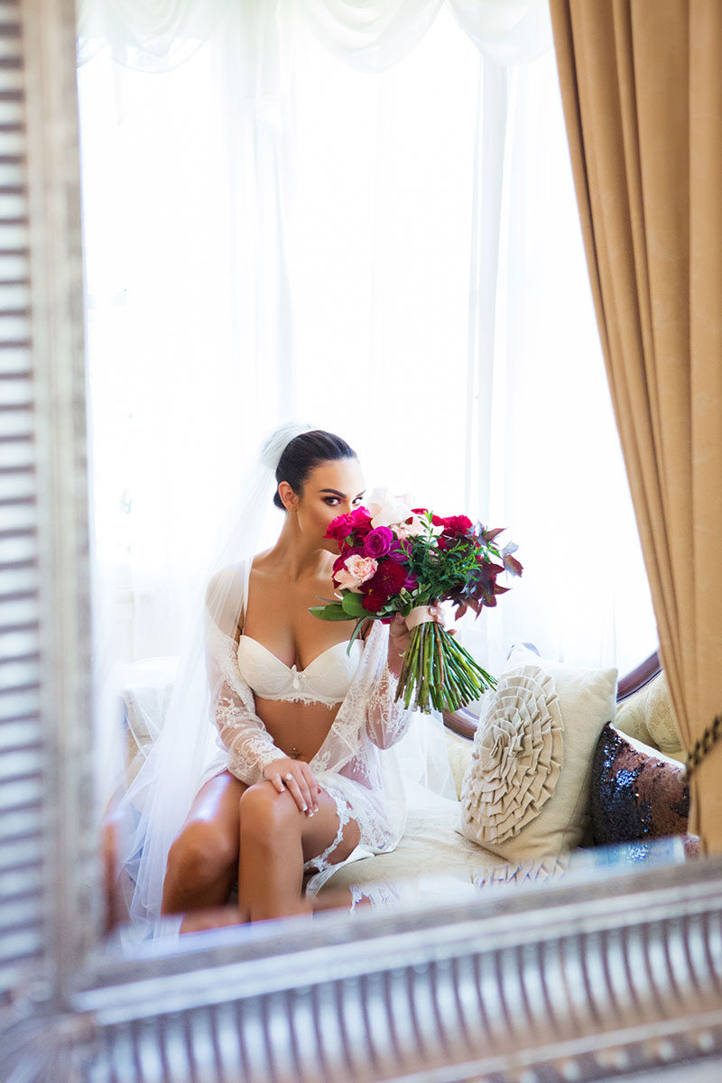 Bride in lingerie and holding flowers while seated.