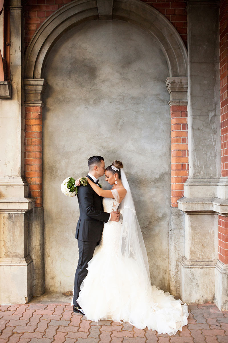 Bride and Groom facing eachother in front of an old brick and concrete wall.