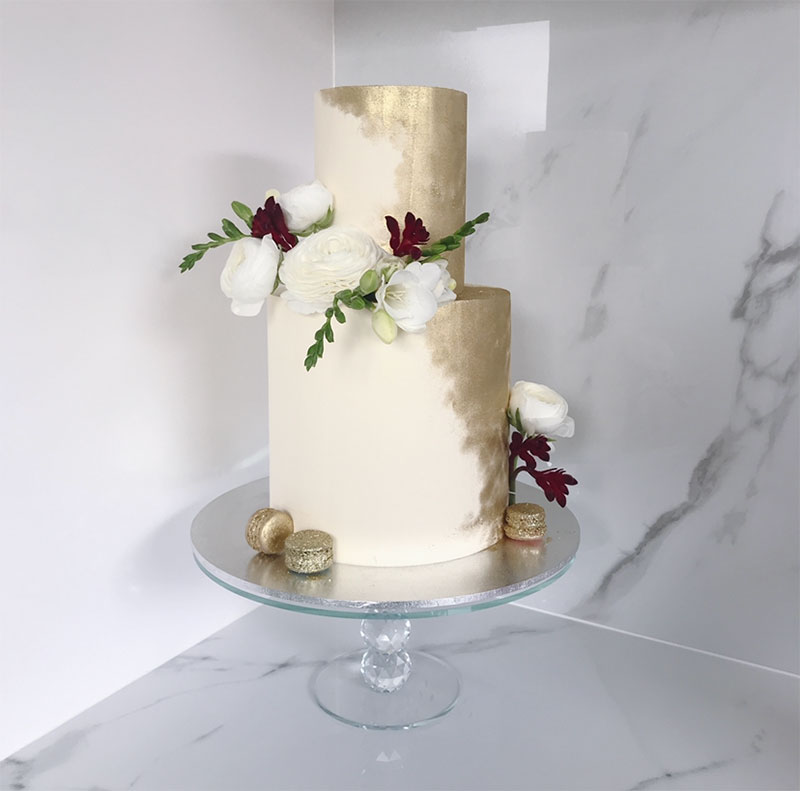 Metallic wedding cake with painted on gold, gold macaroons and flowers.