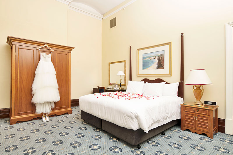 Spacious Deluxe King Room with rose petals on bed at Treasury Brisbane.